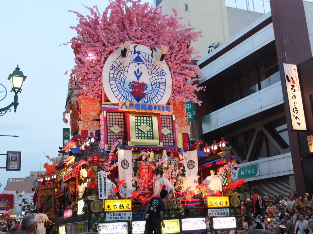 八戶三社大祭的人物山車在傍晚街道展開，沿途有參與者與觀眾