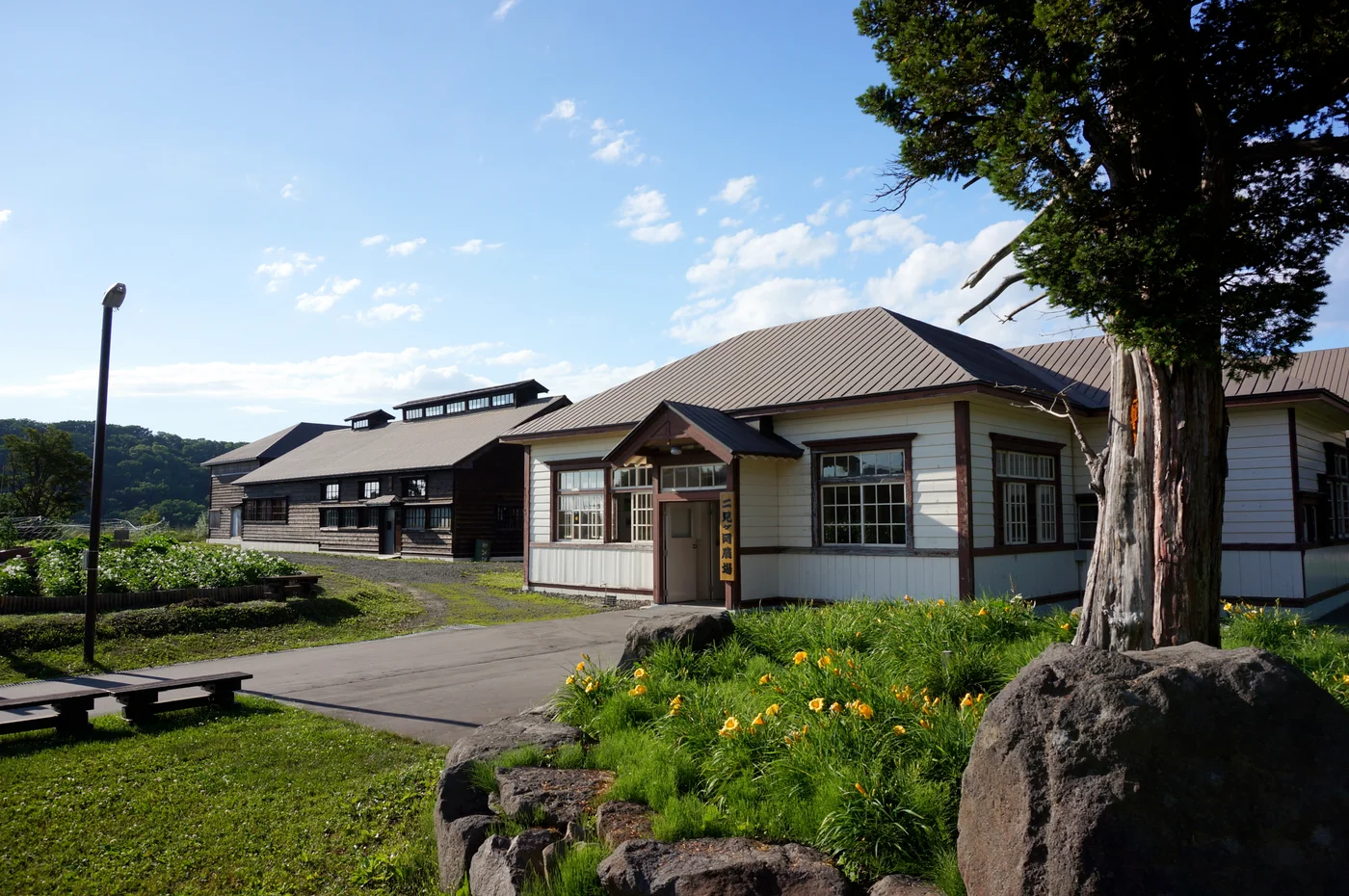 二見ヶ岡農園前方淺色廳舍入口有農場標牌，後方連著深色木造炊場及屋頂排煙構造
