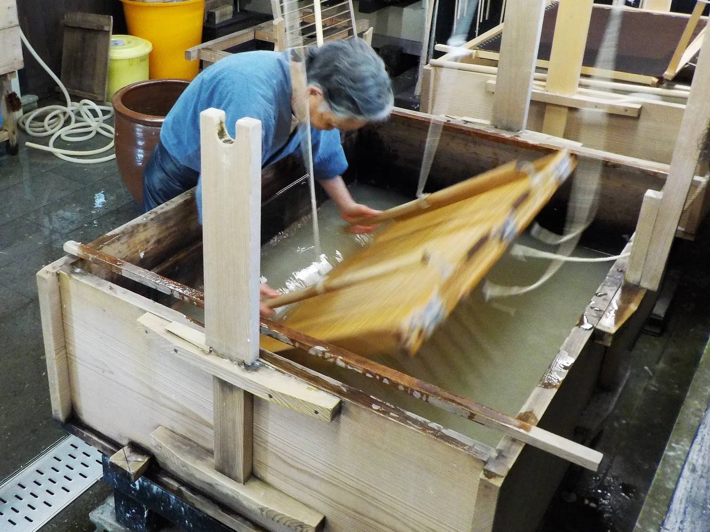 卯立工藝館的職人俯身操作漉桁,框內紙料隨動作流動