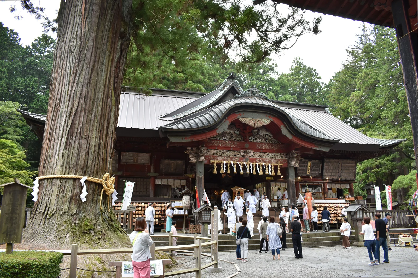 北口本宮冨士淺間神社拝殿的屋頂、木雕與注連繩，參拜者站在建築前方
