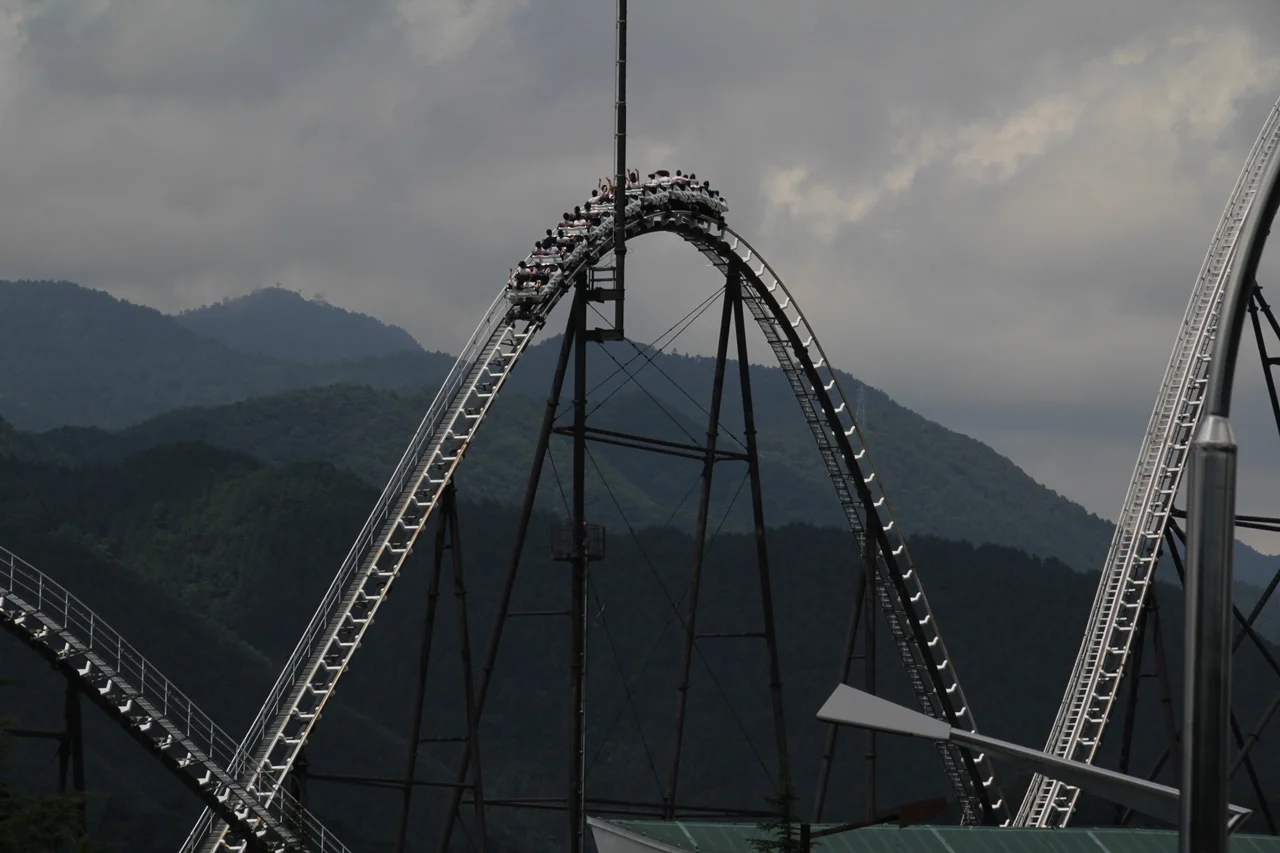 FUJIYAMA 列車越過高架軌道頂部，背景是覆有樹林的山稜與陰雲