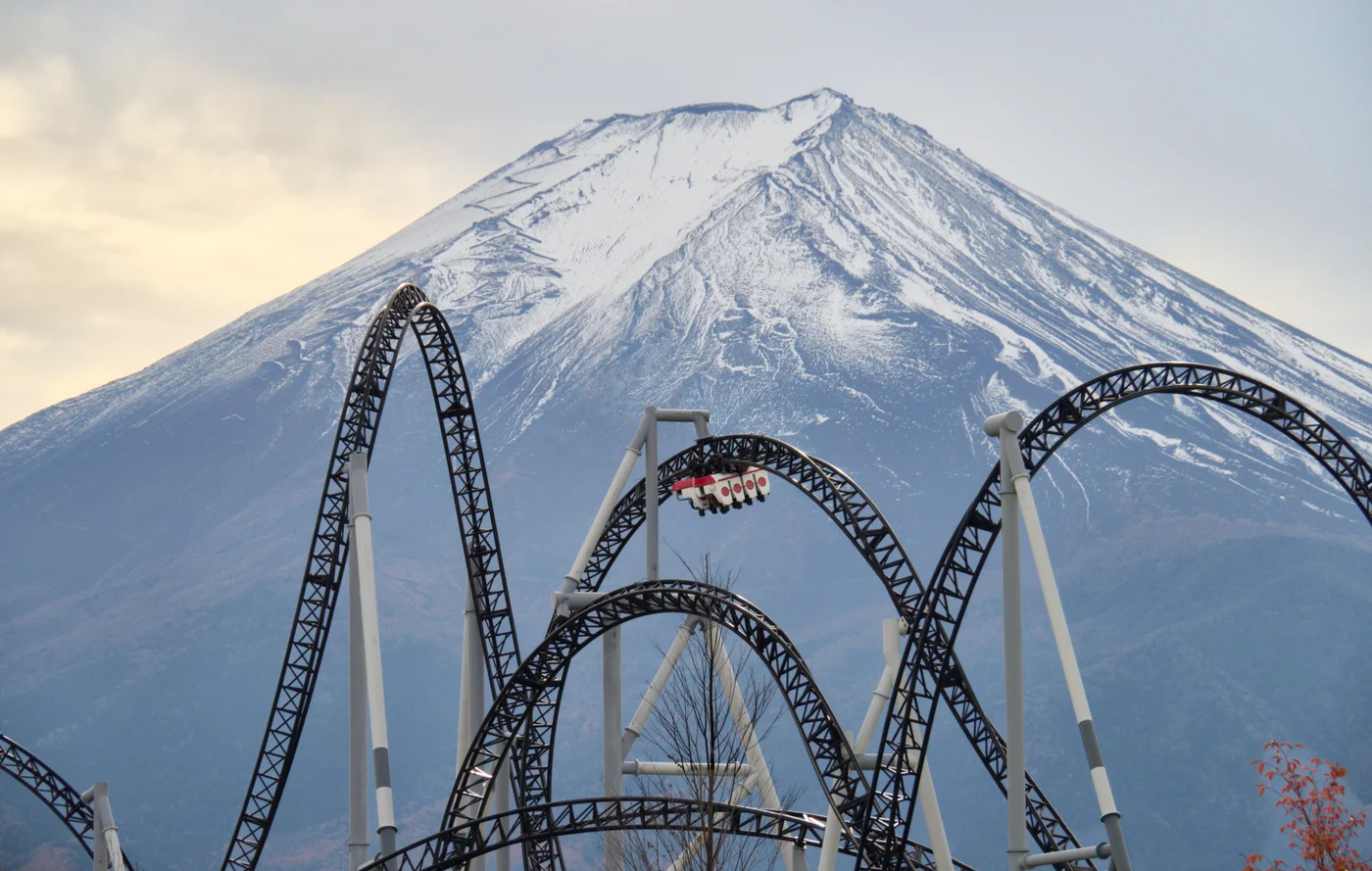 高飛車的黑色軌道、白色支柱與列車，後方是山頂積雪的富士山