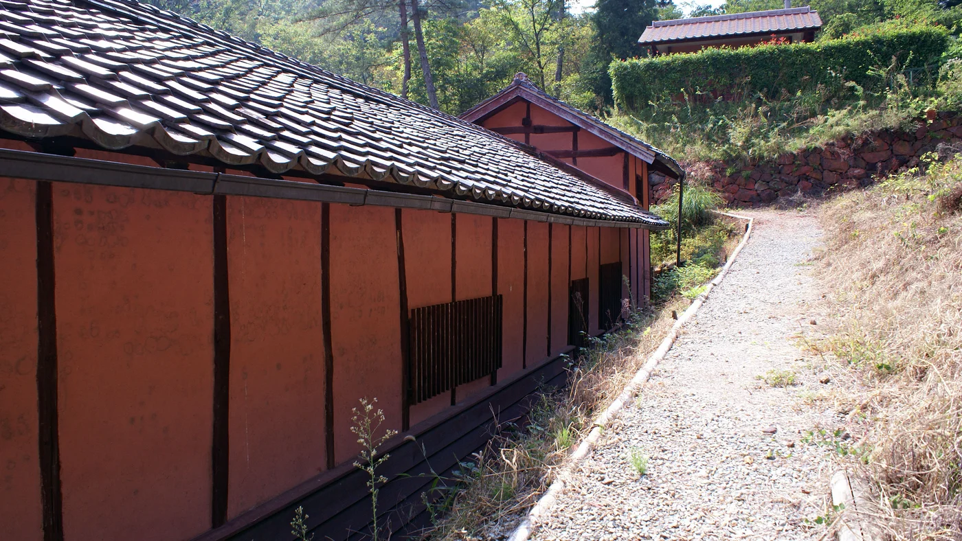 吹屋ベンガラ館的紅色外牆與瓦屋面，旁邊是沿坡向上的碎石步道