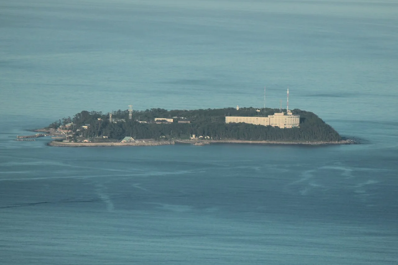 從西北西遠望海面上的初島，可見沿岸建築、綠地與港口