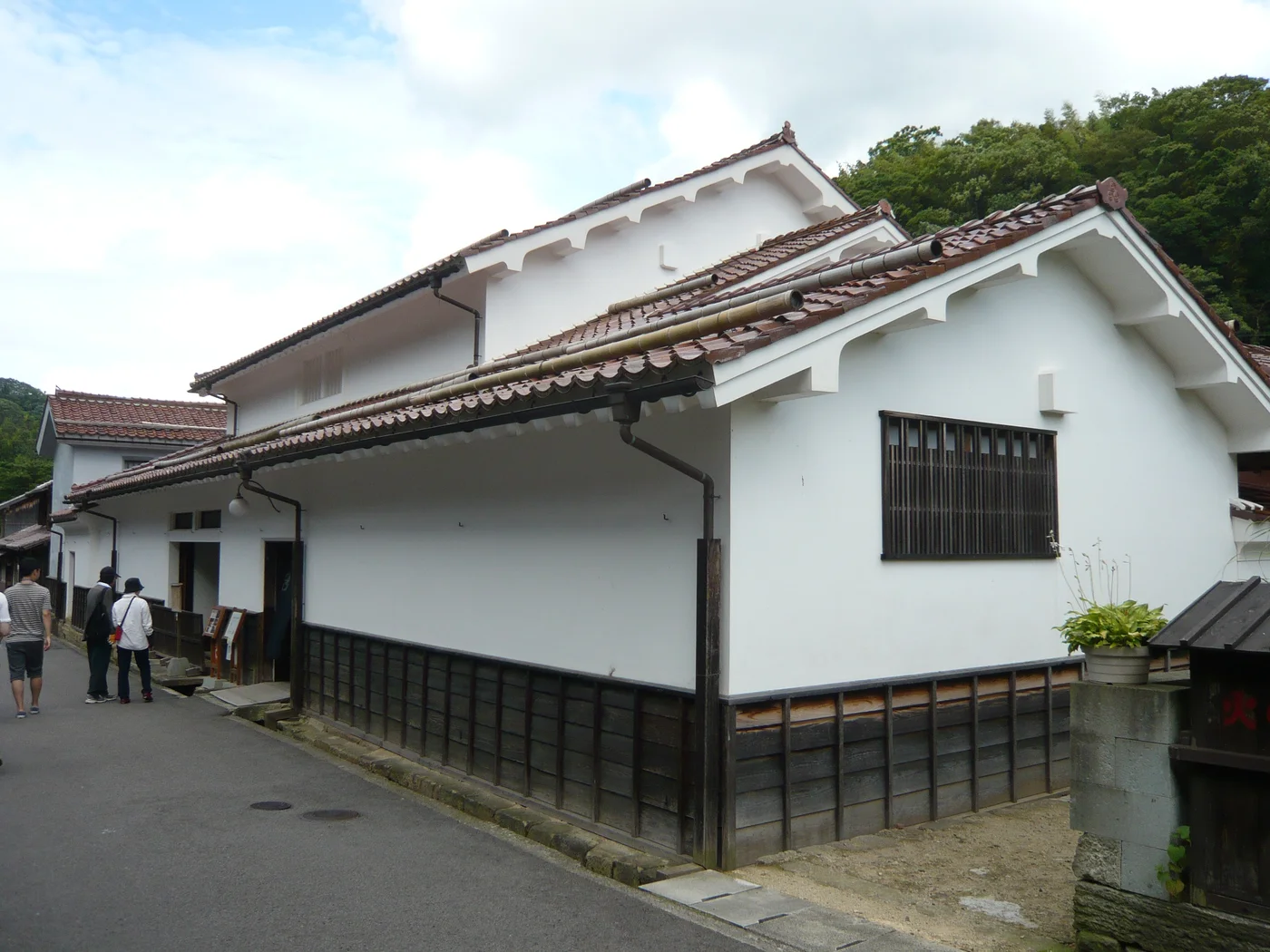 熊谷家住宅的白色外牆、瓦頂與木格窗沿街延伸,左側入口前有遊客。