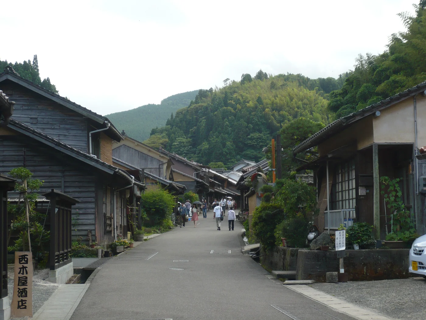大森町的道路兩旁排列木造屋舍,遊客沿街行走,遠方是綠色山林。
