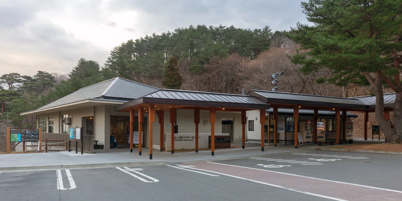 浄土ヶ浜遊客中心的低矮建築與木柱入口雨棚,後方是林地