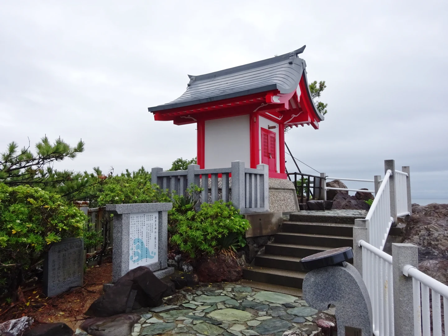 紅白色海津見神社建在龍王岬岩石旁，前方有石階、石欄與扶手
