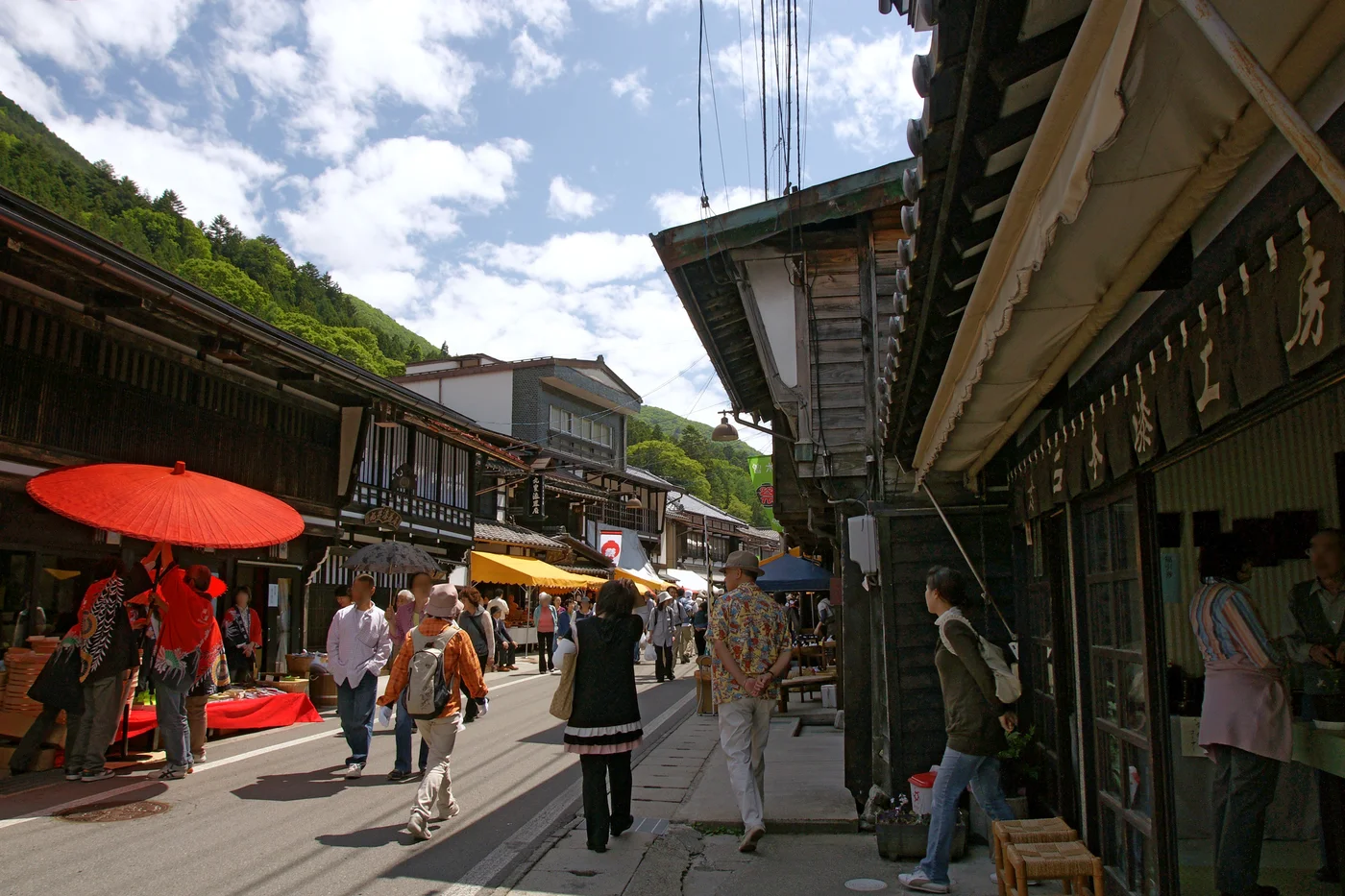 木曽平沢街道兩側的木造店面與深屋簷,左側撐著紅傘,行人沿路逛店