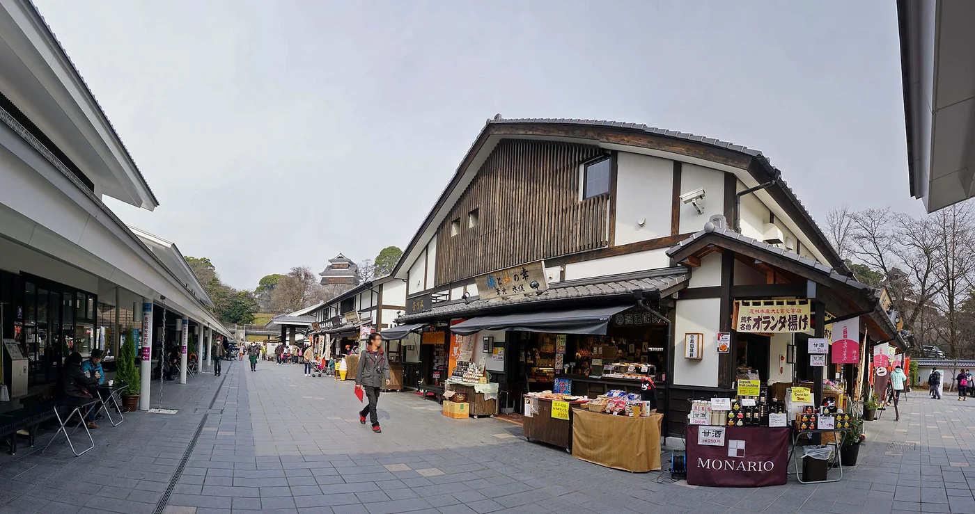 城彩苑的木造商店沿石板步道排列,遠處可見熊本城天守