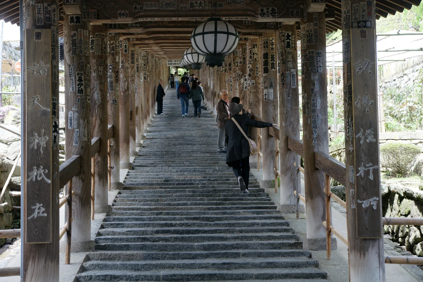 奈良長谷寺登廊的有頂石階向上延伸，木柱掛有奉納札，圓燈籠沿廊道排列。