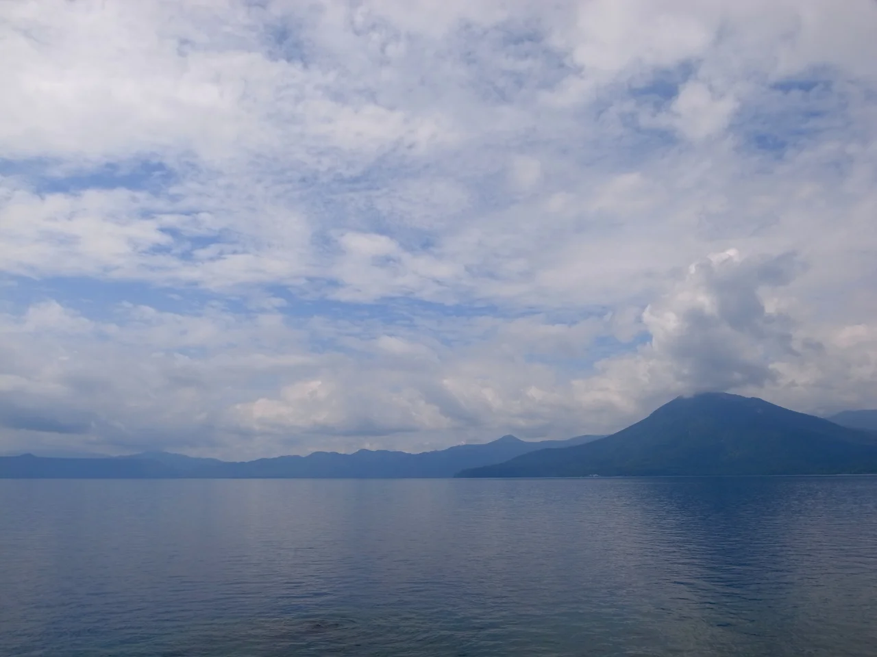 夏季支笏湖平靜湖面、遠方山稜與大片雲層