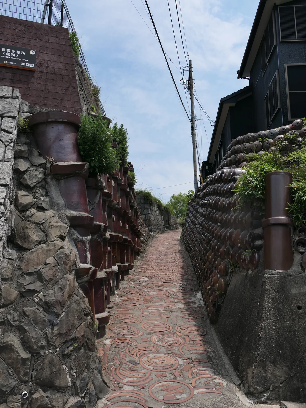 常滑土管坂的窄坡道，左側大型陶管、右側瓶口排列成牆，腳下鋪有圓輪