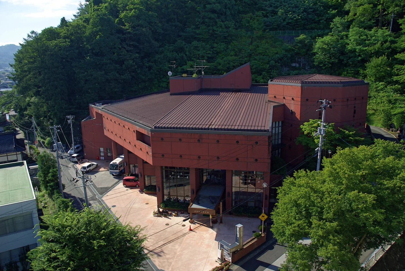 遠野市立博物館紅磚色外觀,入口前方是道路,館舍後方為綠色山林