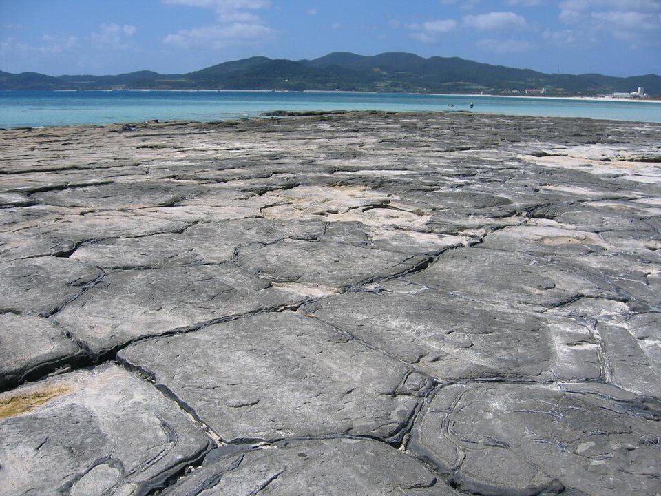 奧武島畳石密集的多角形岩面，後方是海水與久米島山景