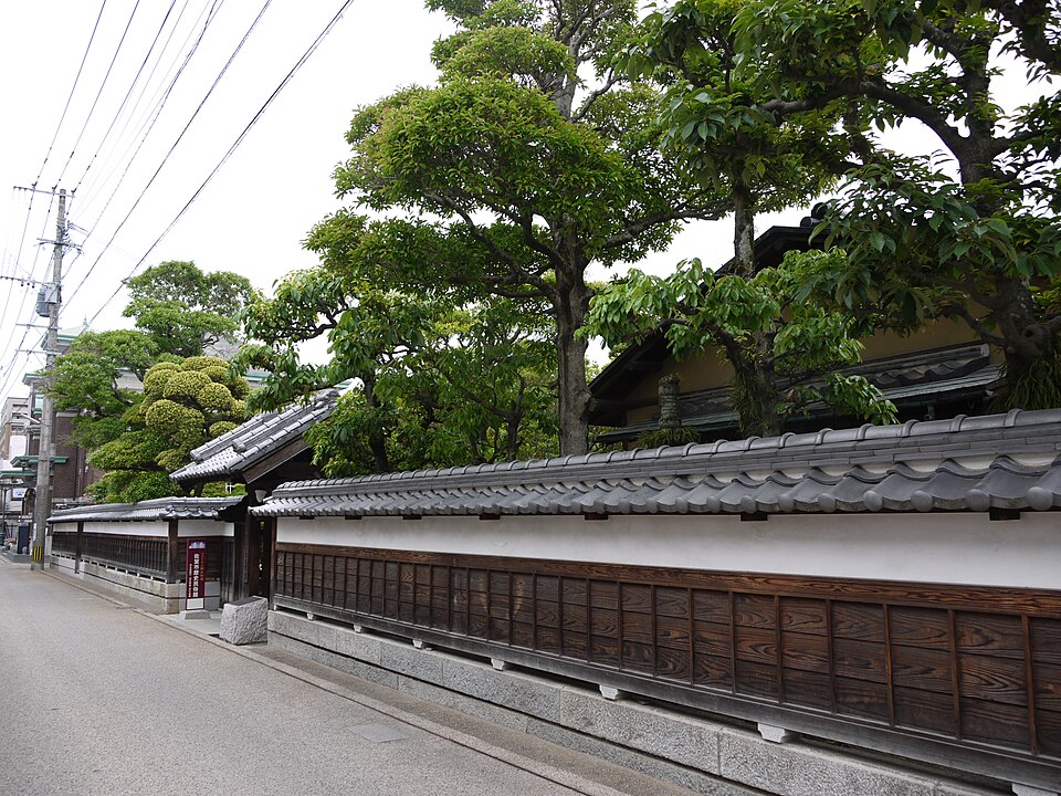 舊古賀家臨街的白牆、瓦簷、綠樹與木門入口