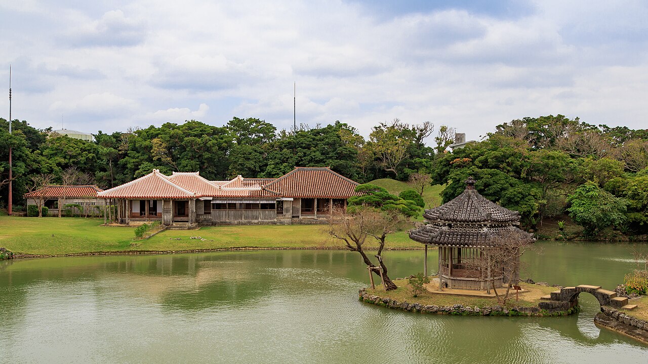 從池岸望向識名園御殿紅瓦屋頂,前方可見六角堂與石拱橋的整體庭園關係