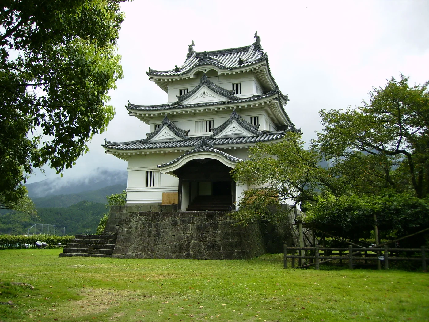 宇和島城白色三層天守立於石垣上,正面可見弧形屋瓦與入口,兩側是綠樹